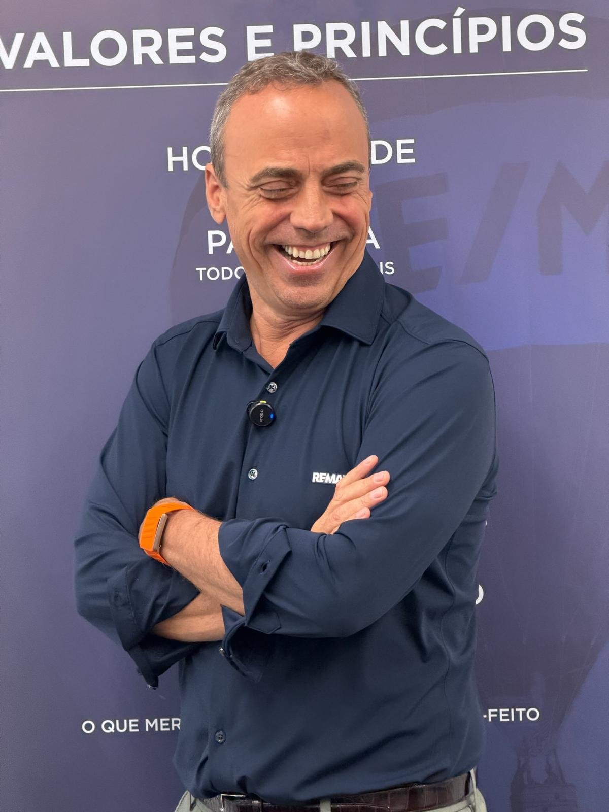 Pedro Fonseca rindo, de braços cruzados, diante do painel Valores e Princípios da RE/MAX