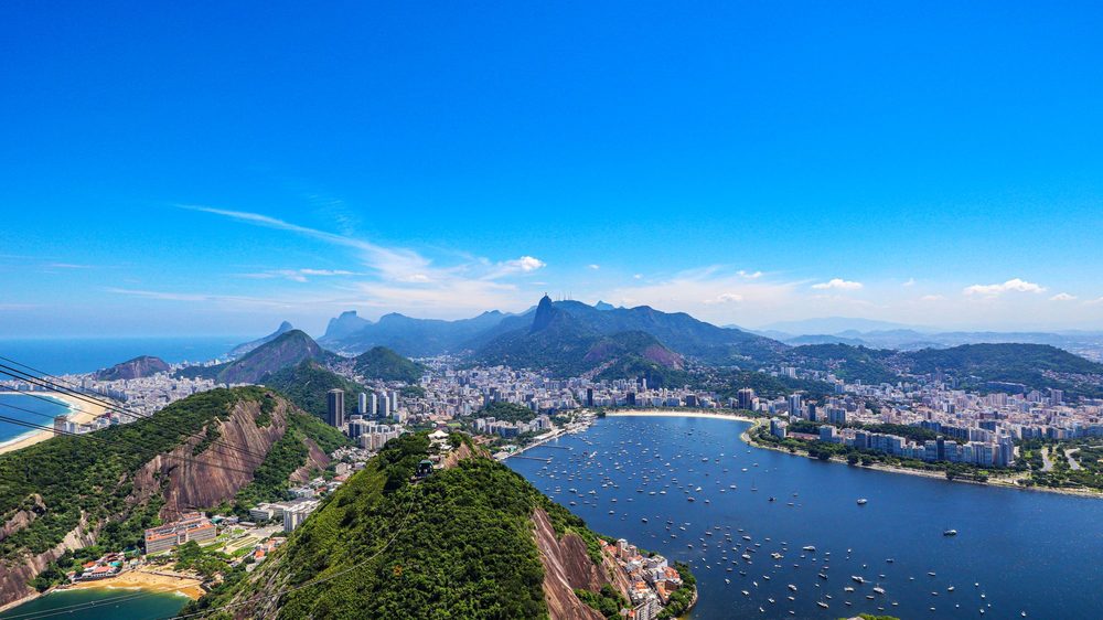 Orla do Rio de Janeiro em dia de céu azul, com os morros e a cidade encontrando o mar